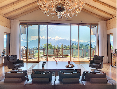 Interno di un appartamento duplex con un bellissimo lampadario e una lussuosa vista sulle montagne attraverso le enormi finestre dal pavimento al soffitto e il balcone.