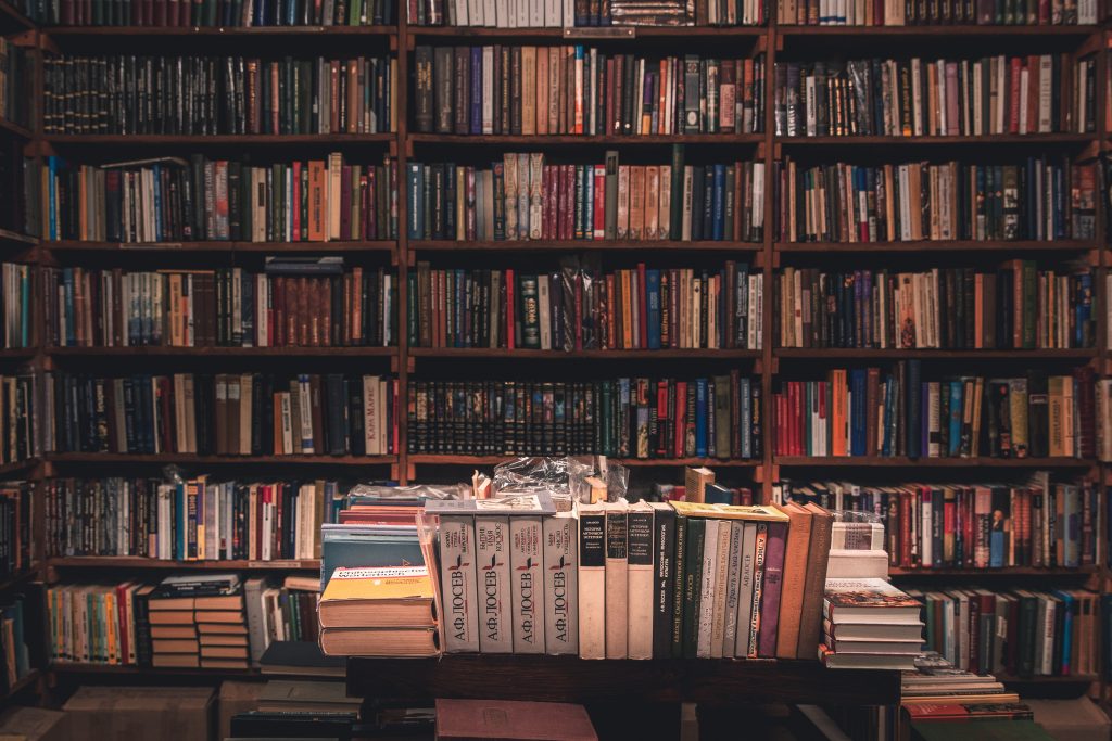 Foto do interior de uma livraria tradicional com paredes cobertas de livros usados coloridos e uma mesa na frente cheia de livros também.