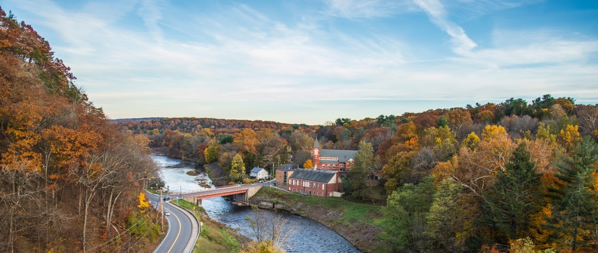 Aerial view over a bridge in Westchester county in a wooded area during Fall; The trees are orange and a red brick house appears in the middle of the picture.