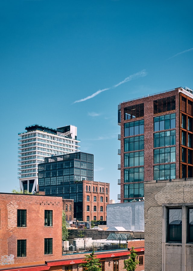 Uma vista de edifícios de diferentes estilos no Brooklyn, com estilo histórico, prédio baixo de tijolos vermelhos na frente e edifícios modernos de vidro ao fundo.