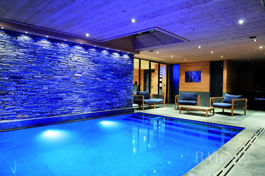Un chalet moderno con piscina, de noche, con luces azules y una acogedora sala de estar al aire libre.