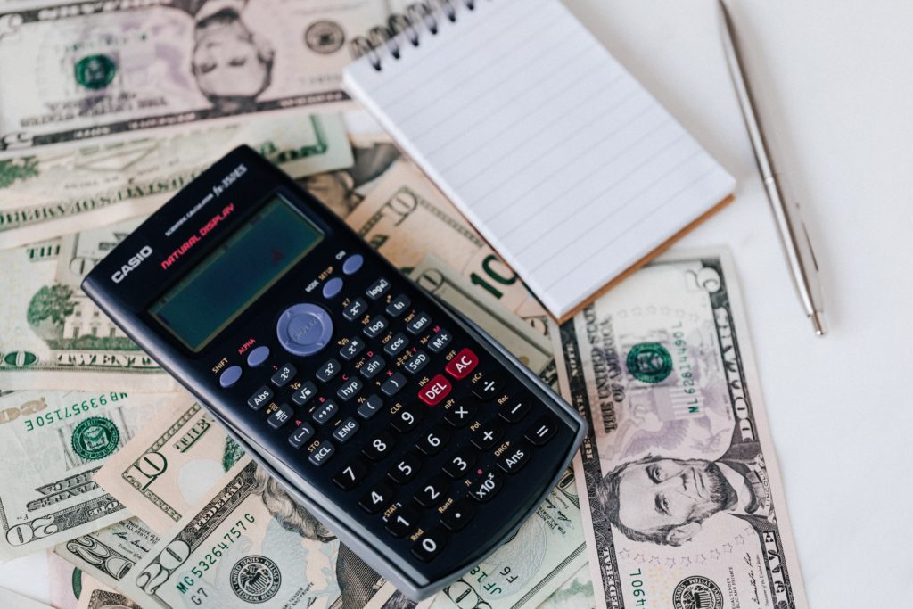Uma calculadora e um bloco de notas ao lado de uma pilha de notas de dólar.