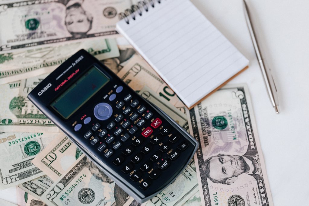 A calculator and a notepad next to a stack of dollar bills.