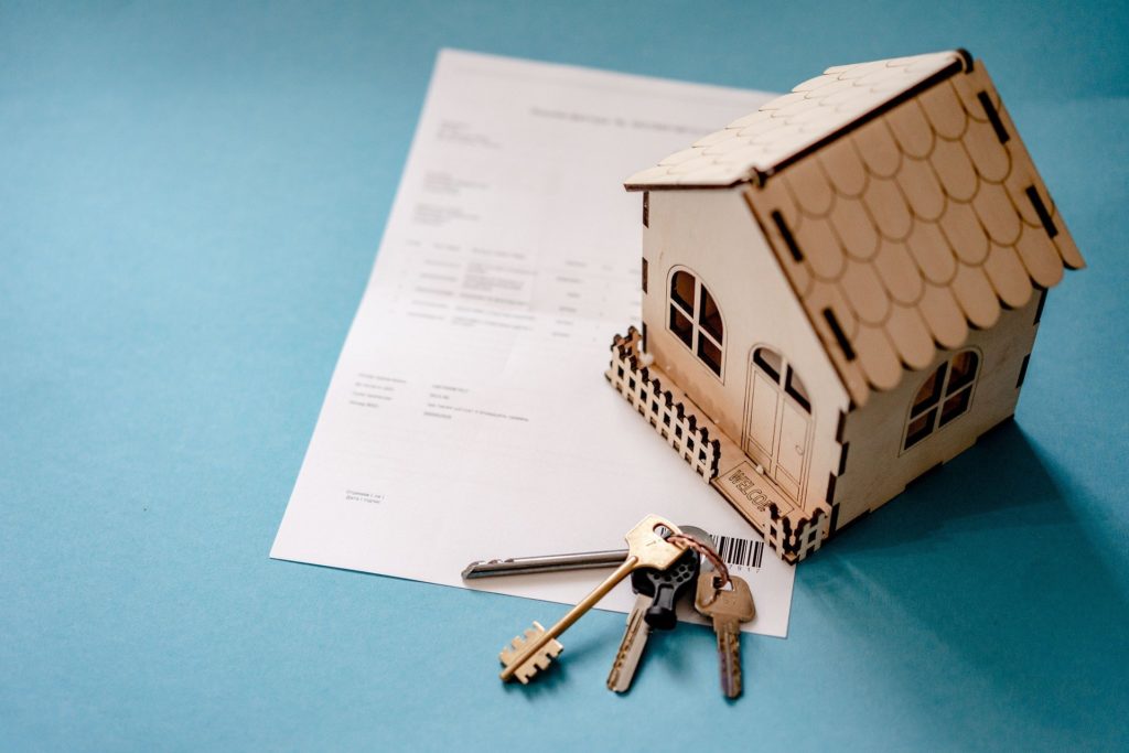 A miniature home next to a set of keys and a piece of paper.