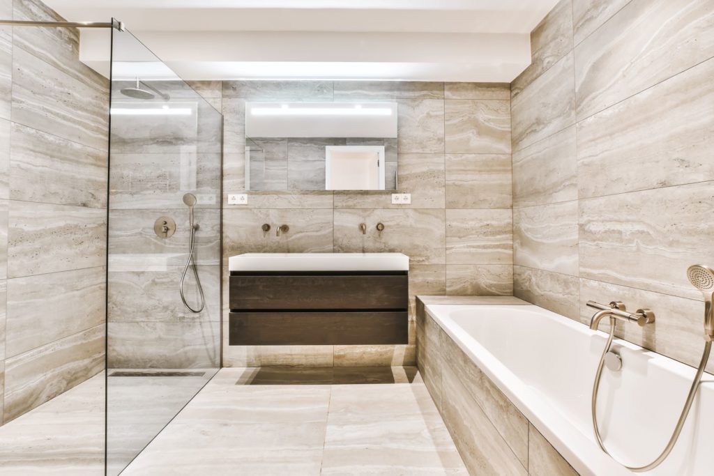 Salle de bain de luxe en marbre marron clair, avec une cabine de douche avec des panneaux de verre et une baignoire.