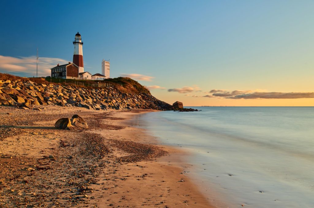 The Montauk lighthouse in the sunset, with the beach in the foreground and the sea.